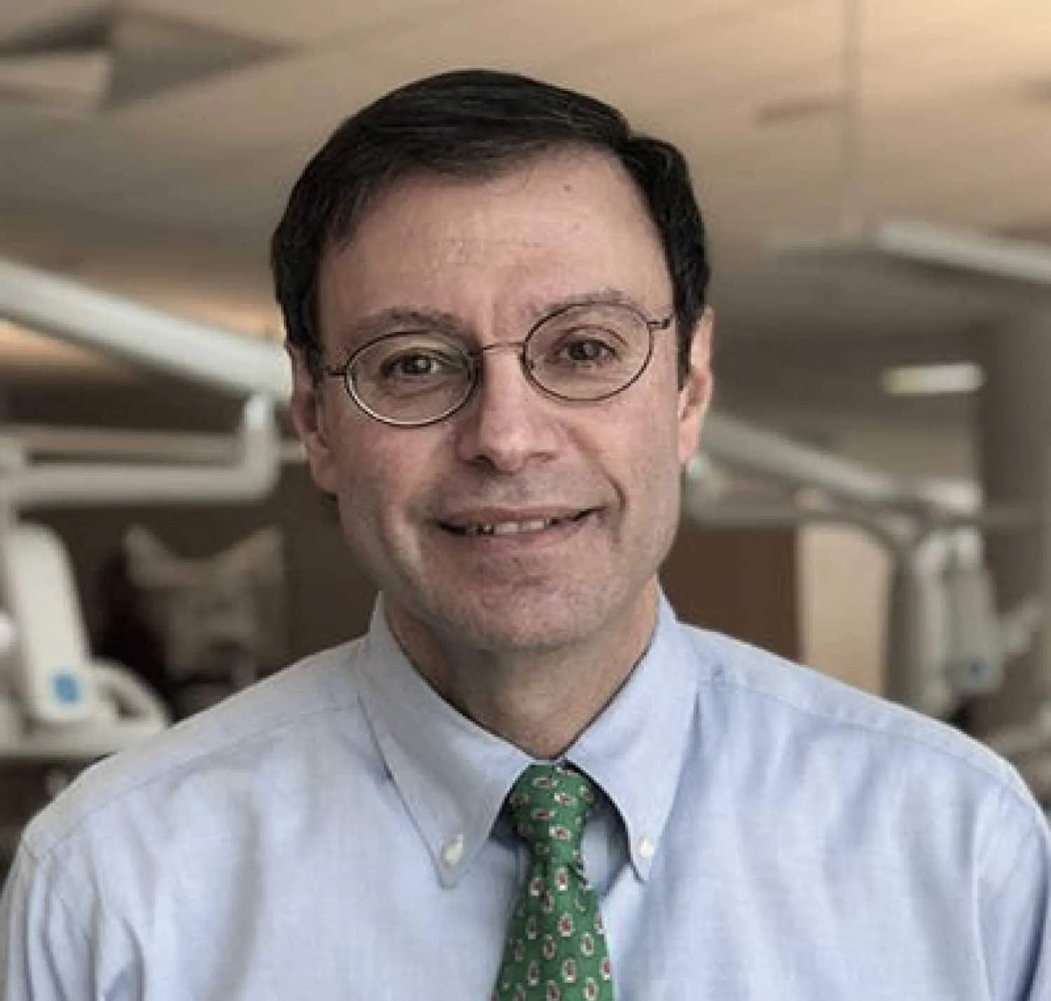 Dr. David Cabeceiras, orthodontist at ARCH Orthodontics, smiling in dental office setting, wearing glasses and a green tie, showcasing expertise and professionalism in orthodontic care.